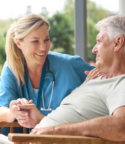 Female Nurse Comforting Depressed Senior Man Sitting In Chair On Home Visit